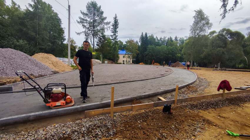 Рабочий с виброплитой уплотняет основание тротуара при благоустройстве территории