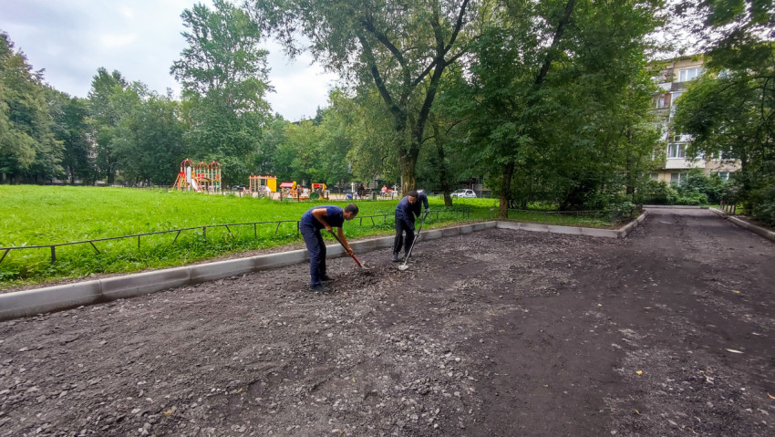Рабочие разравнивают отсыпку щебня и крошки на дворовой дороге перед укладкой покрытия