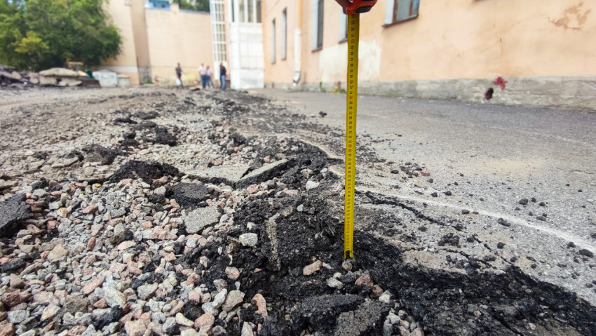 Измерение глубины щебёночной подушки среди обломков асфальта при ремонте покрытия