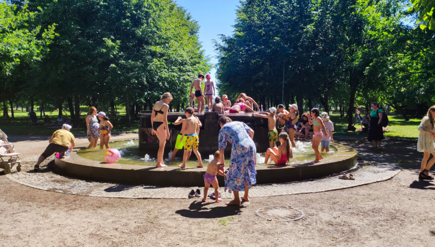 Дети и взрослые отдыхают у круглого фонтана в парке в жаркую погоду