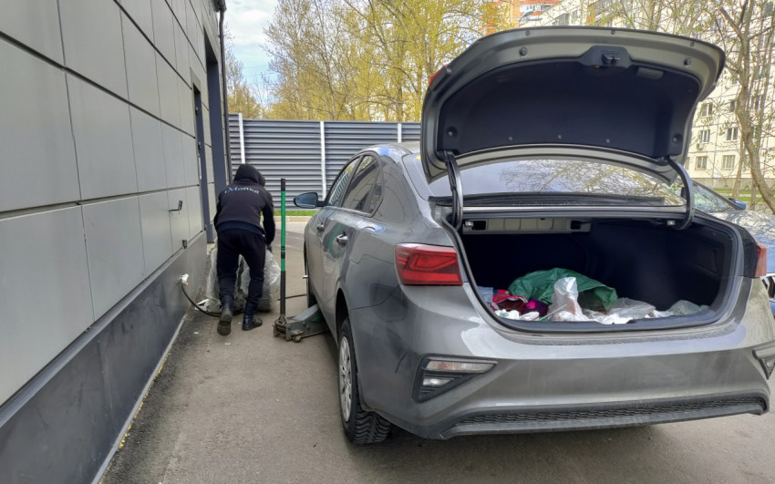 Рабочий перемещает упакованное колесо возле автомобиля