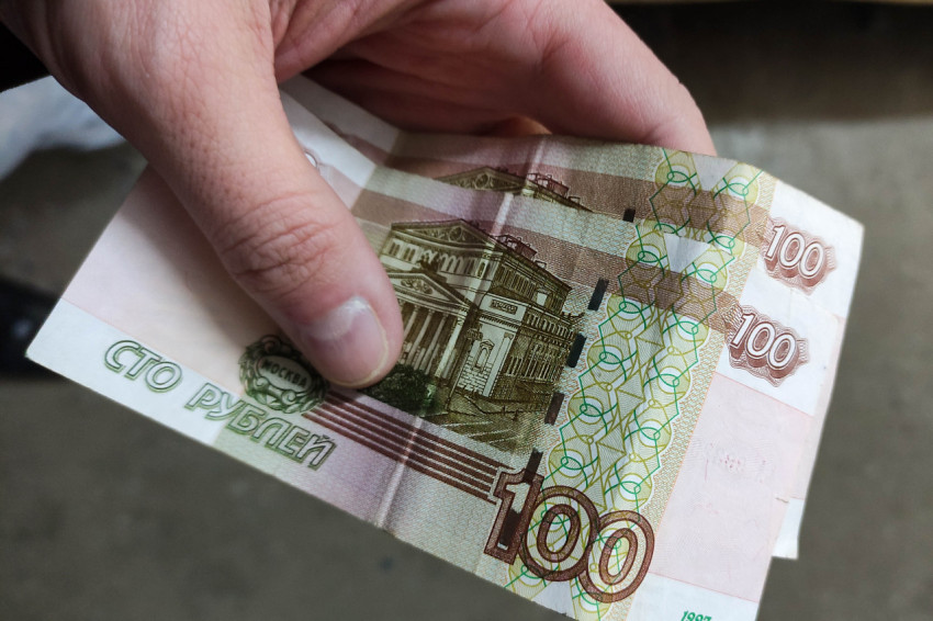 Рука держит несколько купюр номиналом 100 рублей