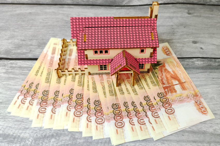 Модель дома на фоне купюр номиналом 5000 рублей