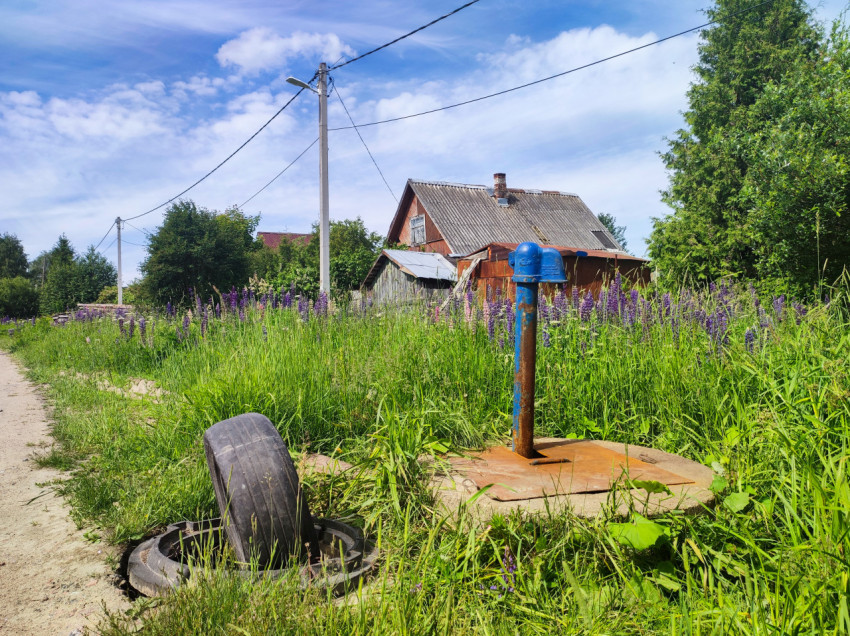 Уличная водоразборная колонка и открытый люк у деревенского дома