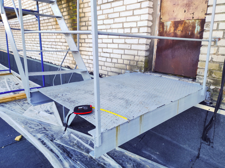 Металлическая площадка лестницы с рулеткой у ржавой двери на кирпичной стене