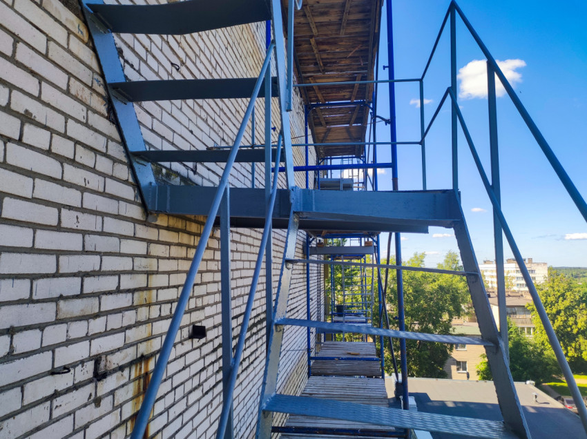 Площадка строительных лесов у кирпичной стены с видом на деревья и дома