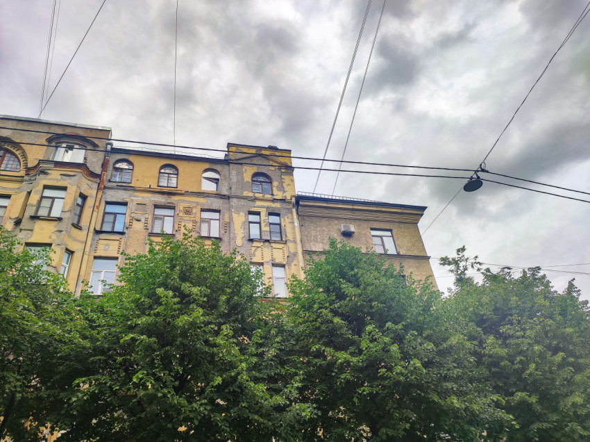 Верхние этажи старого жилого дома с облупившейся штукатуркой и проводами