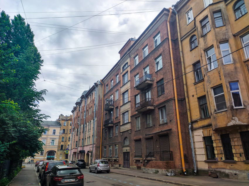 Узкая улица Санкт-Петербурга с многоэтажными жилыми домами, припаркованными машинами и проводами контактной сети