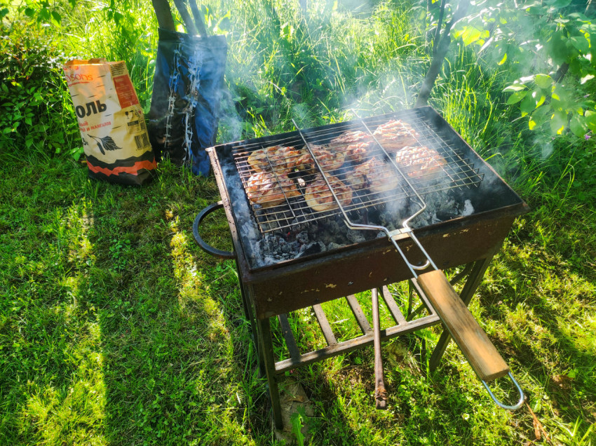 Мангал с курицей на решётке и дымом на траве рядом с мешком угля