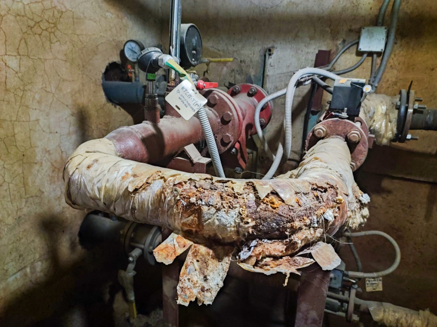 Корродированный узел трубопровода с манометром и проводкой в техническом помещении