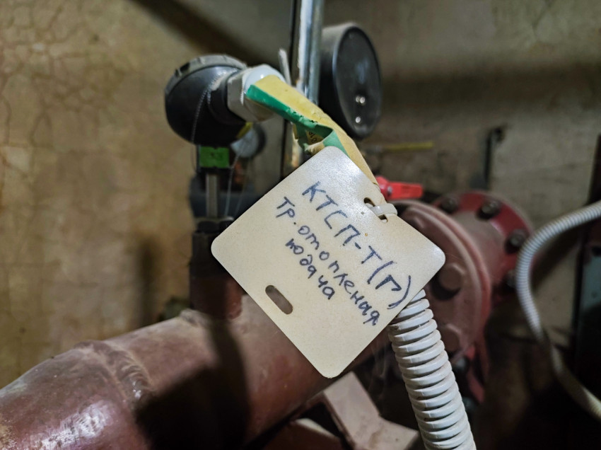 Маркировочная бирка с рукописной надписью на трубопроводном датчике крупным планом