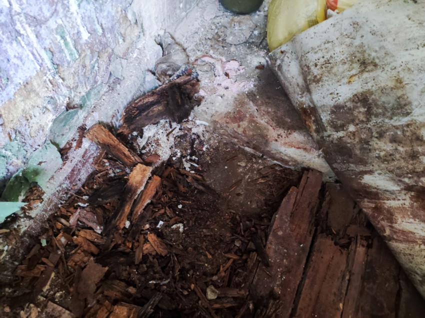 Разрушенный участок деревянного пола у стены с осыпавшейся штукатуркой