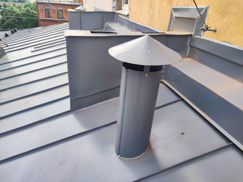Вентиляционная труба с защитным зонтом на металлической крыше рядом с коробами