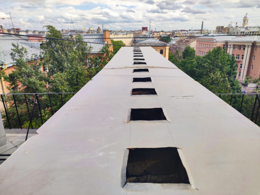 Ряд прямоугольных проёмов на плоской металлической кровле с видом на город
