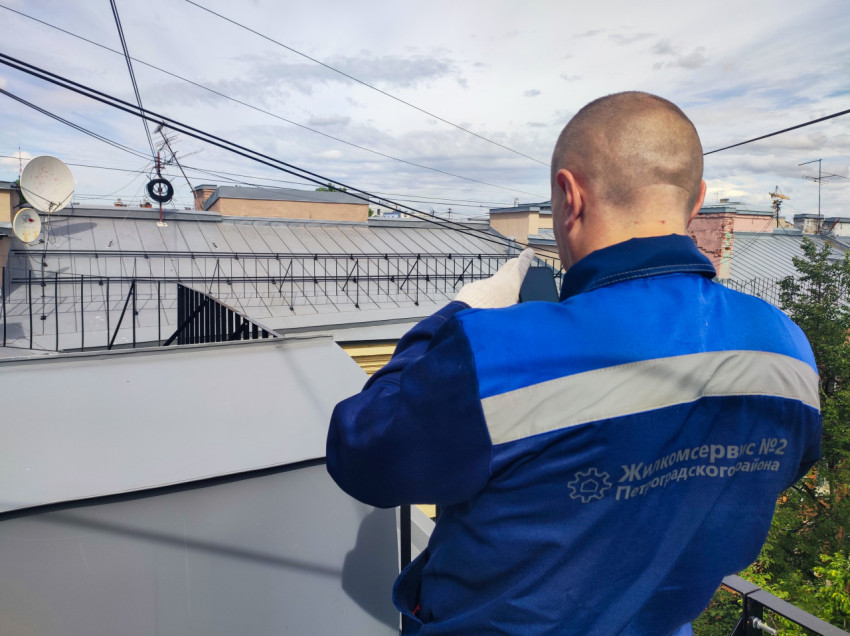 Работник в форме делает фото или фиксацию на крыше рядом с кабелями и антеннами