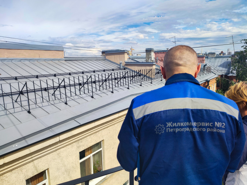 Сотрудник «Жилкомсервис №2 Петроградского района» на крыше на фоне снегозадержателей и труб