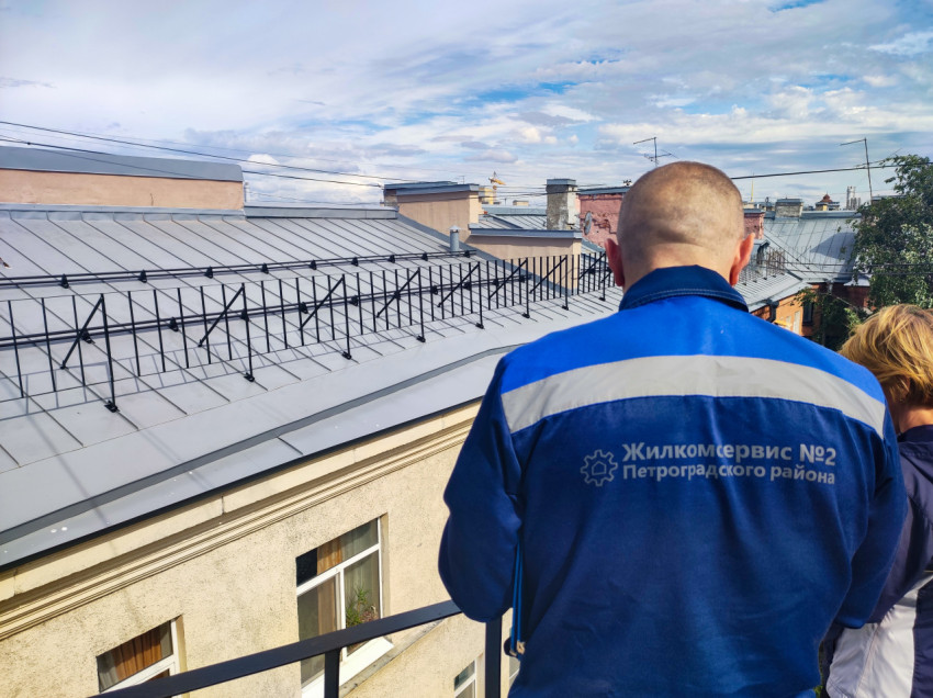 Сотрудник коммунальной службы на крыше дома с ограждением и снегозадержателями