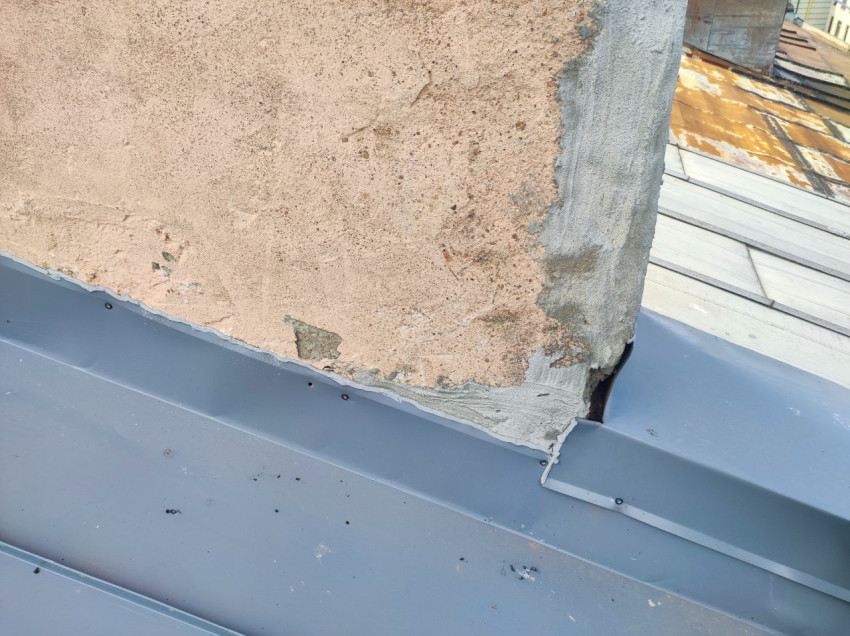 Деталь примыкания кровельного фартука к стене с повреждённой штукатуркой и зазором