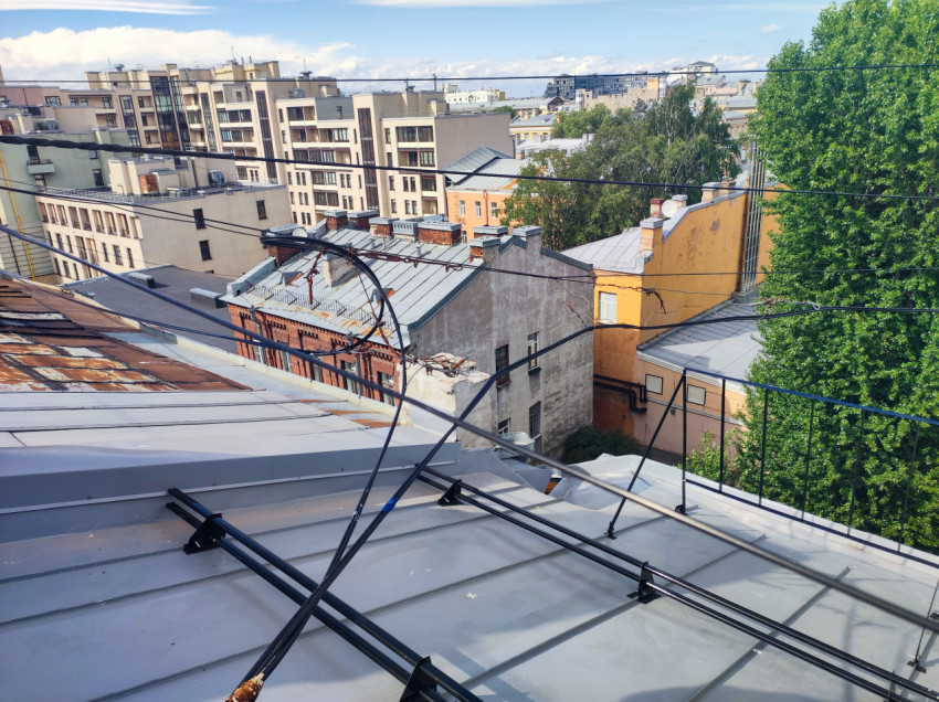 Крыши квартала и фасады домов, пересечённые воздушными кабелями, на фоне современных жилых корпусов