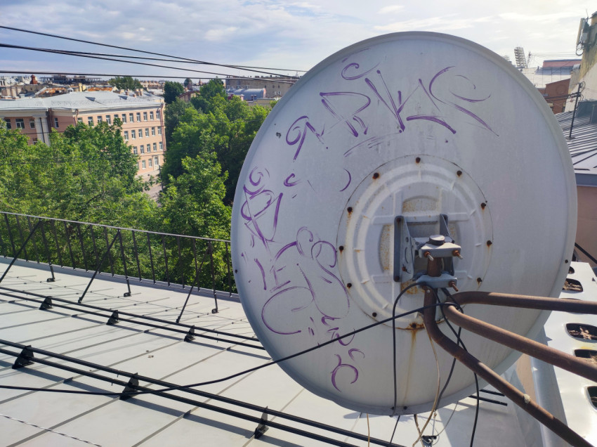 Спутниковая тарелка с надписями на крыше на фоне деревьев и домов