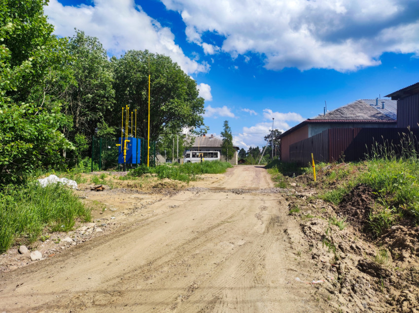 Песчаная дорога в посёлке и ограждённая площадка с синим шкафом и жёлтыми трубами