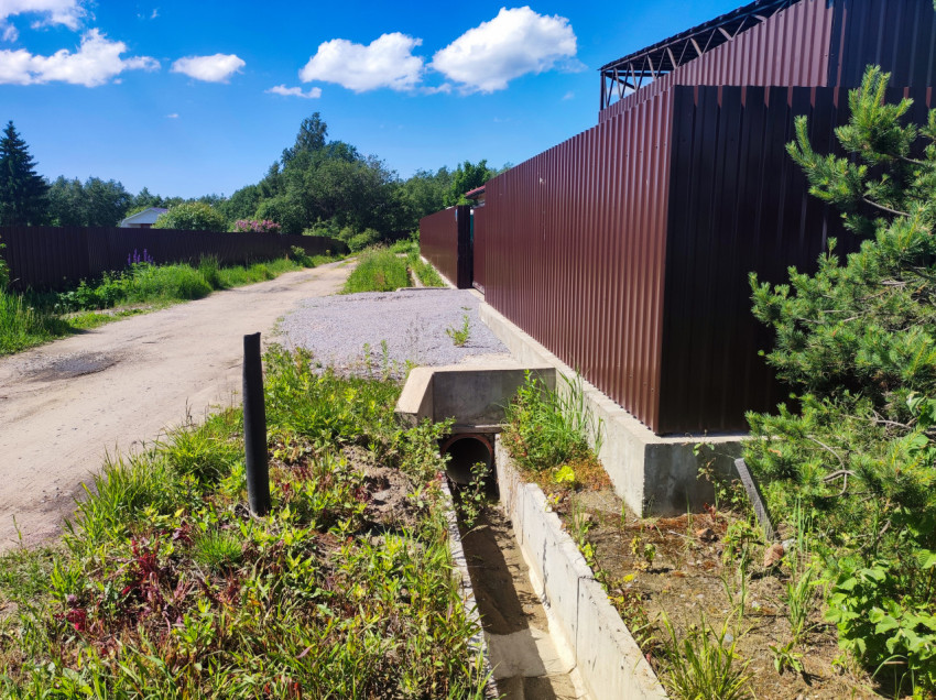 Водоотводная канава с трубой под заездом во двор рядом с забором из профлиста