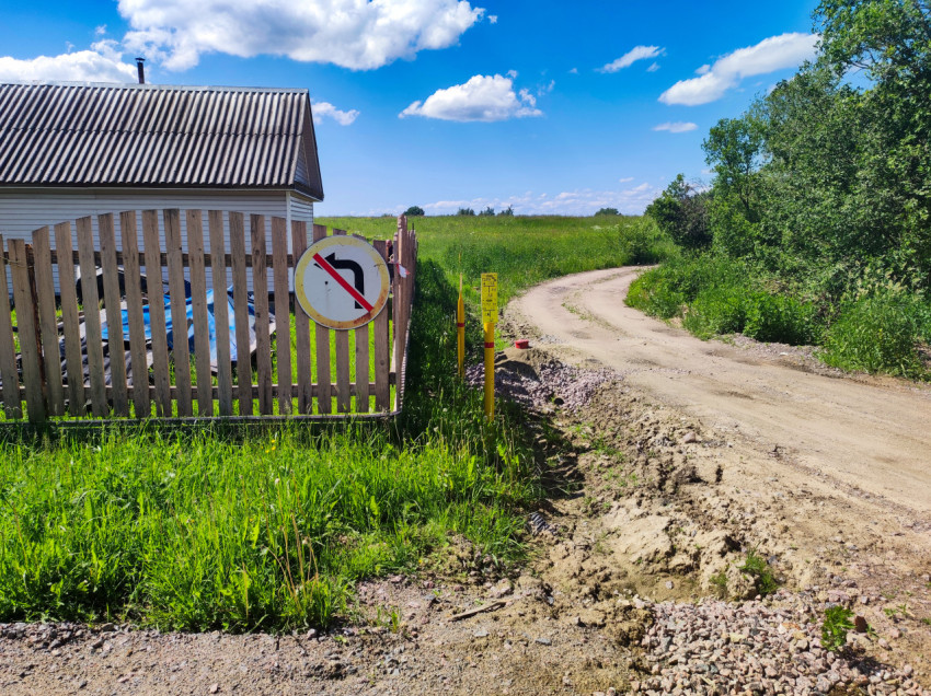 Дорожный знак «поворот налево запрещён» на заборе у грунтовой дороги и поля