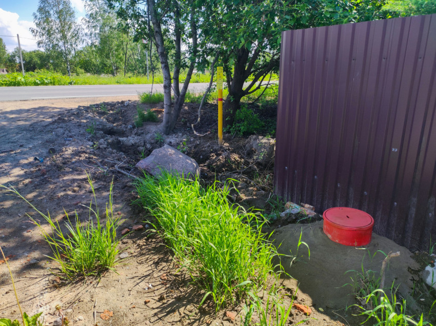 Крышка колодца у забора и сигнальный столбик коммуникаций на обочине асфальтированной дороги
