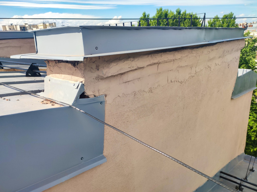 Крупный план оштукатуренного парапета с металлическим колпаком и креплением отливов на кровле