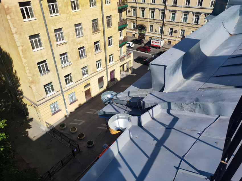 Вид с крыши на водосборные воронки и металлические скаты над двором с жилыми фасадами и припаркованными машинами