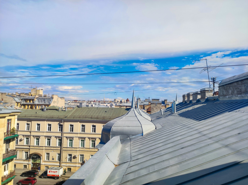 Панорама городских крыш с фальцевой кровлей, декоративным куполом и проводами на фоне облачного неба