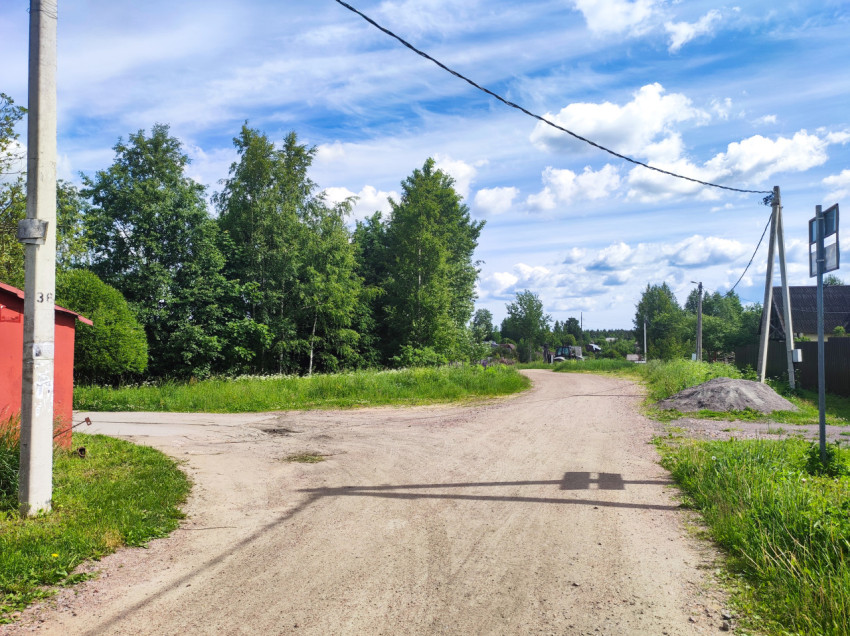 Грунтовый перекрёсток в деревне с опорами ЛЭП, проводами и кучей щебня у обочины