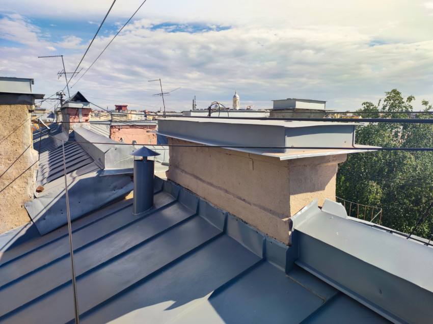 Фальцевая кровля с вентиляционной трубой, парапетами и антеннами на фоне городской линии горизонта