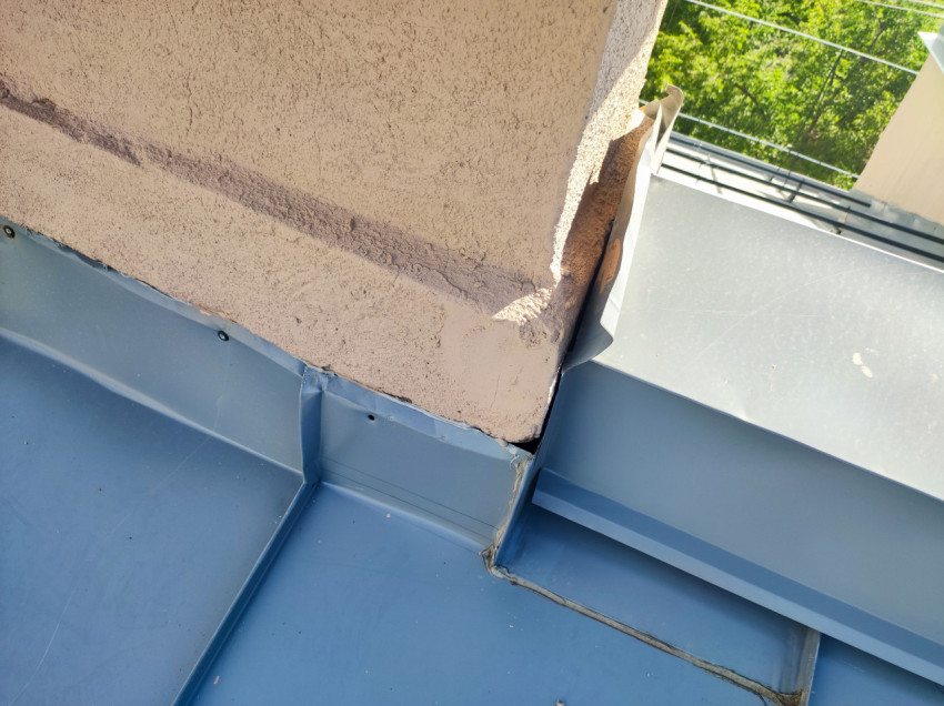 Примыкание стены к кровле и коробу парапета с металлическими фартуками на фоне зелёных деревьев и проводов