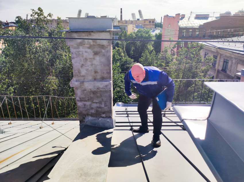 Рабочий на металлической кровле рядом с дымовой трубой и кабелями