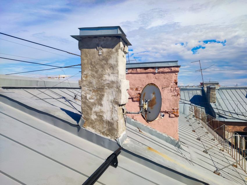 Дымовые трубы и спутниковая антенна на фальцевой крыше под облачным небом