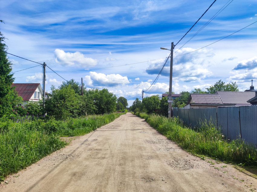 Сельская грунтовая улица с уличным светильником, домами и металлическим забором