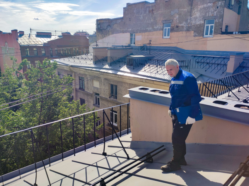 Рабочий на крыше у вентиляционной шахты и ограждения кровли