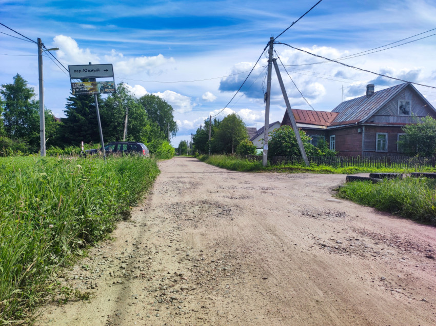 Указатель «пер. Южный» на перекрестке грунтовых дорог рядом с деревянными домами