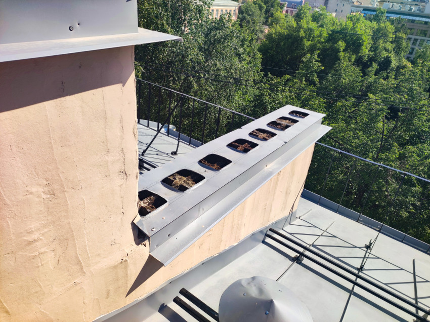 Вентиляционная шахта с накладкой и отверстиями на крыше рядом с дымовой трубой