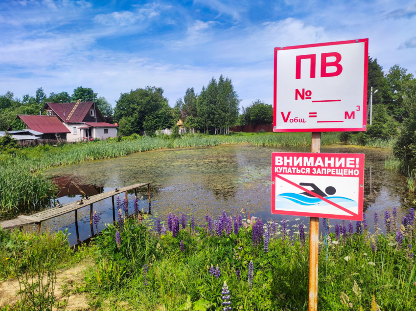 Крупный план табличек «ПВ» и «Купаться запрещено» на берегу сельского пруда