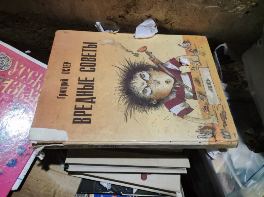 Обложка книги «Вредные советы» среди старых книг и бытового мусора в подвале