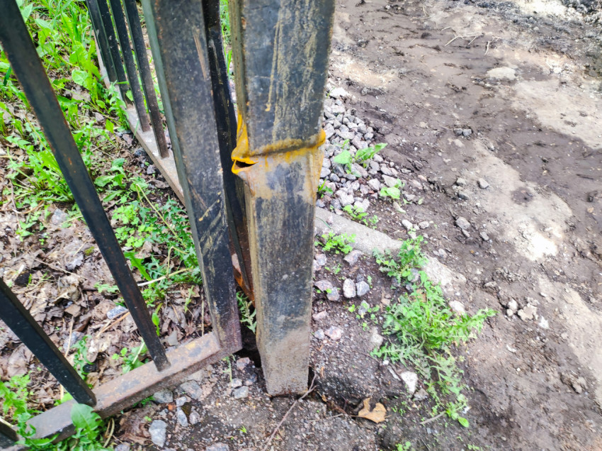 Вмятина на металлическом столбе ограждения на фоне грунта и щебня