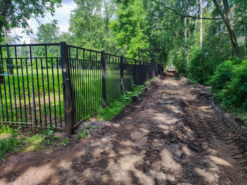 Грунтовая дорога вдоль металлического забора у зелёной зоны и жилых домов
