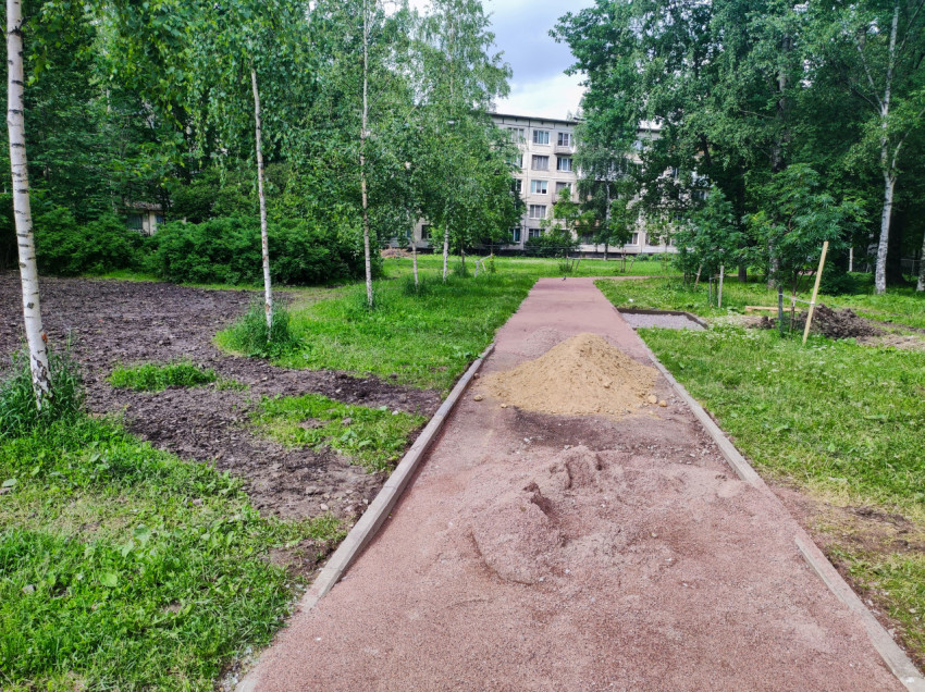 Пешеходная дорожка с бордюрами и кучами песка при работах по благоустройству двора