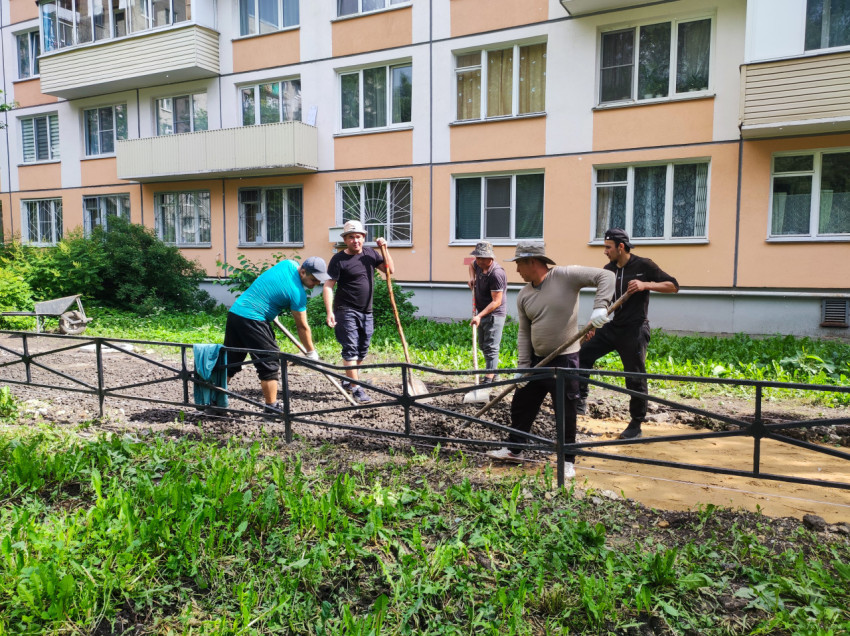 Рабочие с лопатами разравнивают щебень на дворовой дорожке у жилого дома