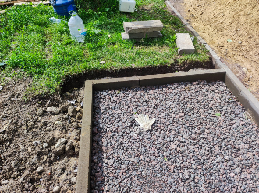 Площадка со щебнем в бетонном бордюре и рабочая перчатка на засыпке