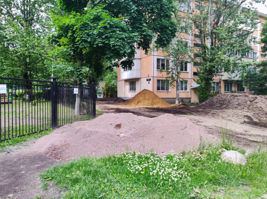 Кучи щебня, песка и грунта во дворе рядом с ограждением и жилым домом