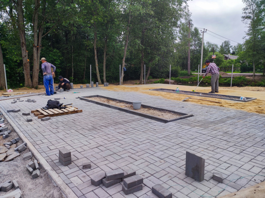 Рабочие укладывают серую тротуарную плитку на песчаное основание