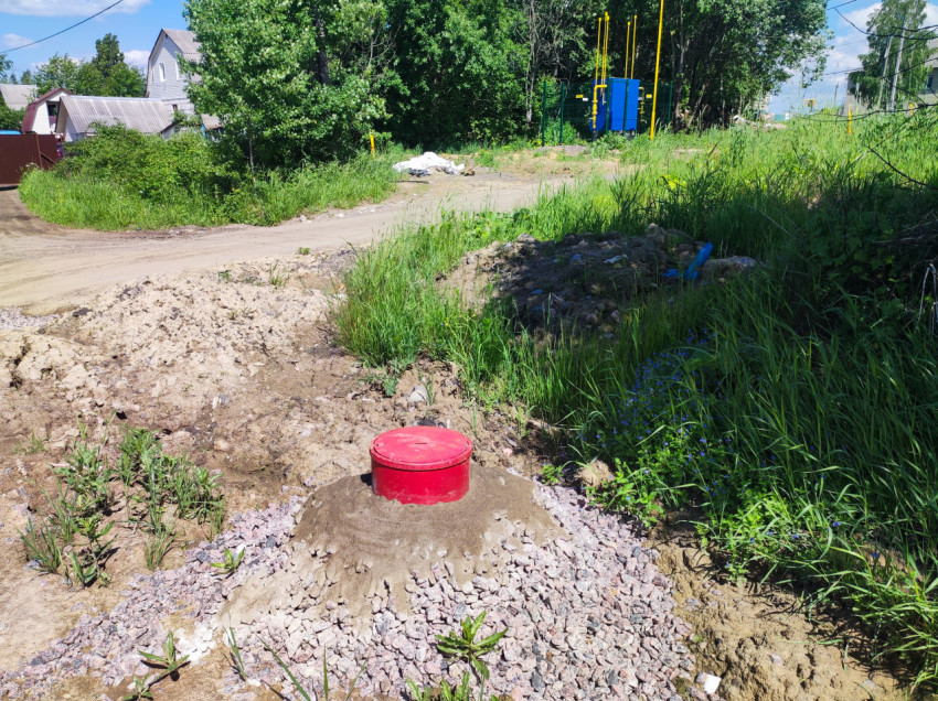 Красная крышка колодца на насыпи из песка и щебня у грунтовой дороги